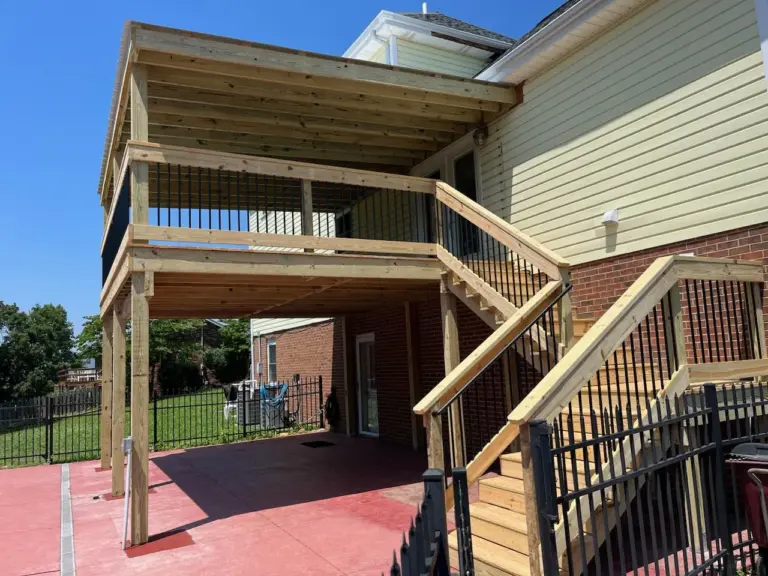 Covered deck with black metal balusters above a red concrete patio