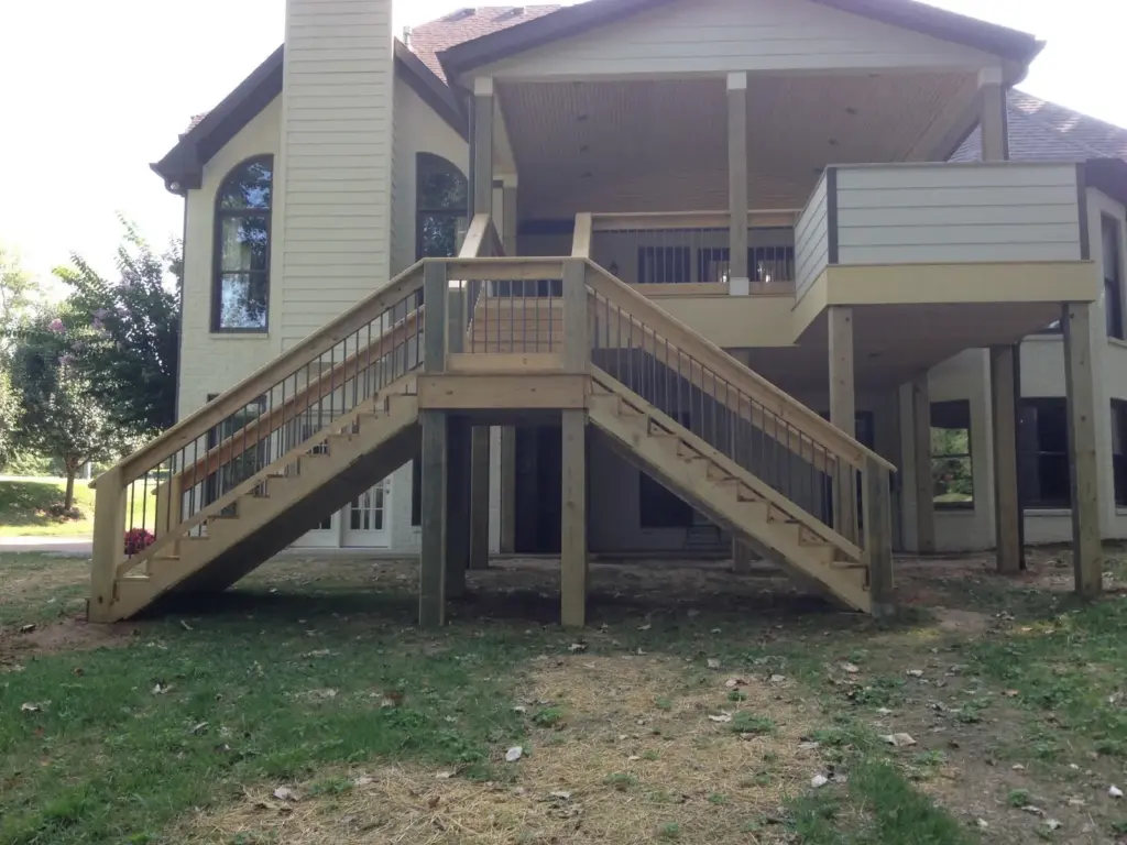 Covered deck with wood railing and stairs descending to the side yard