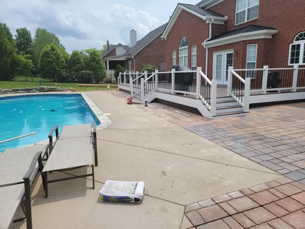 Poolside deck with white railing and paver patio beside an in-ground pool